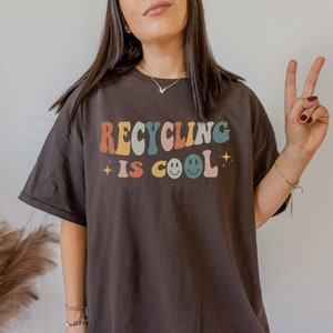 K&ouml;nnte beinhalten: Ein braunes T-Shirt mit dem Text "Recycling is cool" in bunten Retro-Buchstaben mit einem Smiley.