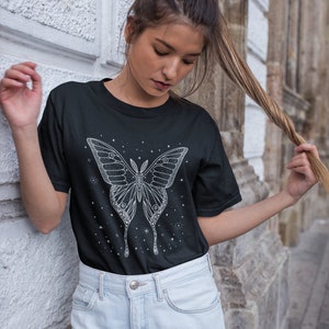 May include: A black t-shirt with a white graphic of a butterfly with stars. The butterfly has intricate details and is surrounded by small stars.
