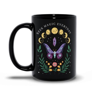 May include: Black ceramic mug with a white design featuring a purple and pink butterfly, a crystal, and a crescent moon phase. The text "SEEK MAGIC EVERYDAY" is printed around the design.