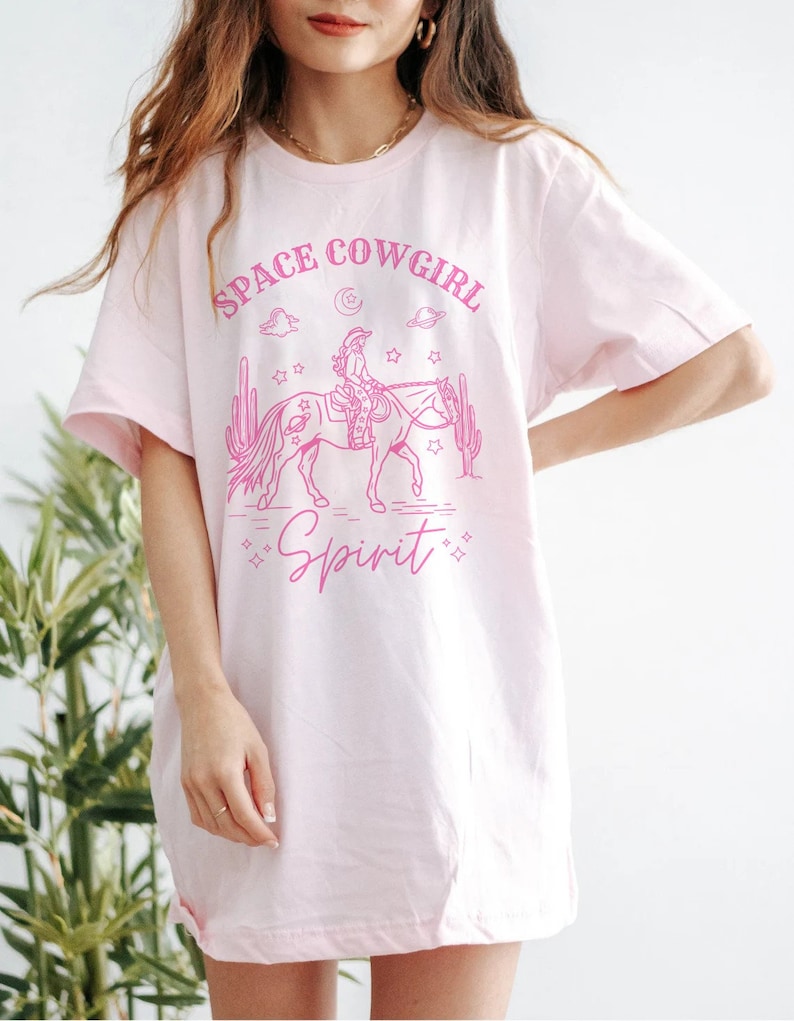 May include: Pink oversized t-shirt with a graphic of a cowgirl riding a horse in front of cacti and stars. The text "Space Cowgirl Spirit" is printed on the shirt.