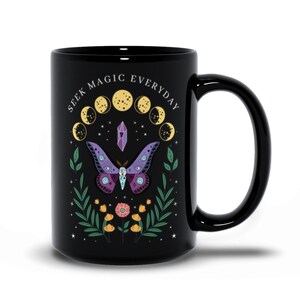 May include: Black ceramic mug with a white design featuring a purple butterfly with eyes, a crystal, and a crescent moon phase. The text "Seek Magic Everyday" is written around the design.