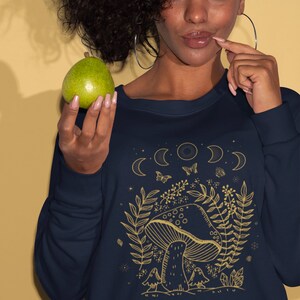 Op de afbeelding: Een marineblauw sweatshirt met een gouden afbeelding van een paddenstoel, bladeren en manen. De tekst "Shroom Queens" staat onderaan de afbeelding gedrukt.