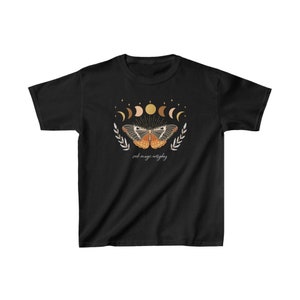 Peut inclure: T-shirt noir avec un motif de papillon aux ailes orange et brun, entour&eacute; d'un croissant de lune et d'&eacute;toiles. Le texte "seek magic everyday" est imprim&eacute; sous le papillon.