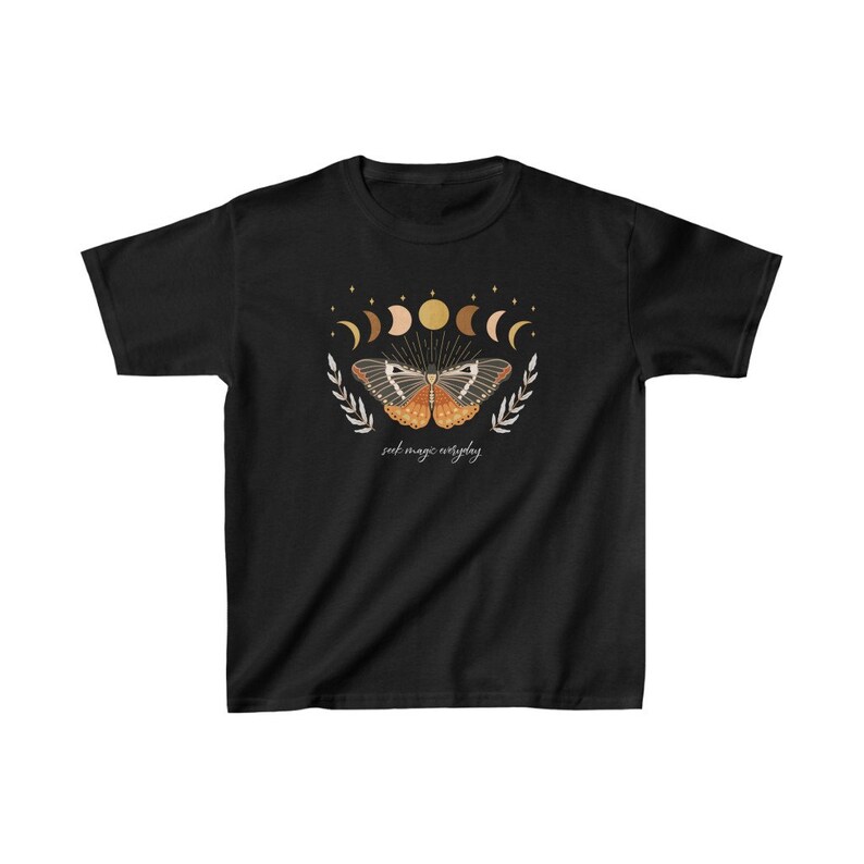 Peut inclure: T-shirt noir avec un motif de papillon aux ailes orange et brun, entour&eacute; d'un croissant de lune et d'&eacute;toiles. Le texte "seek magic everyday" est imprim&eacute; sous le papillon.