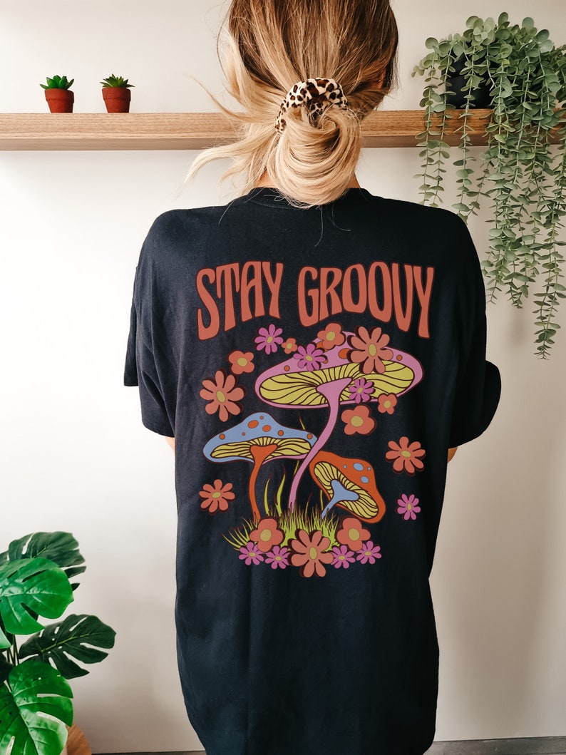 May include: Black t-shirt with a graphic of colorful mushrooms and flowers. The text "STAY GROOVY" is printed in red on the shirt.