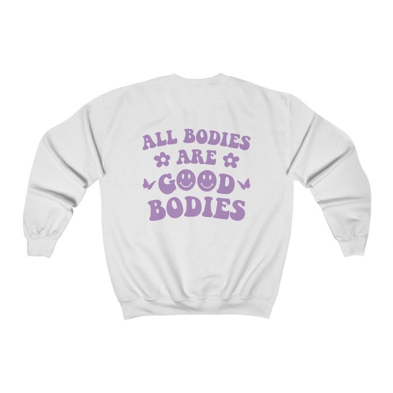 May include: White sweatshirt with the text "ALL BODIES ARE GOOD BODIES" in purple. The text includes flower and butterfly graphics, and two smiley faces. The sweatshirt has long sleeves and a crew neck.
