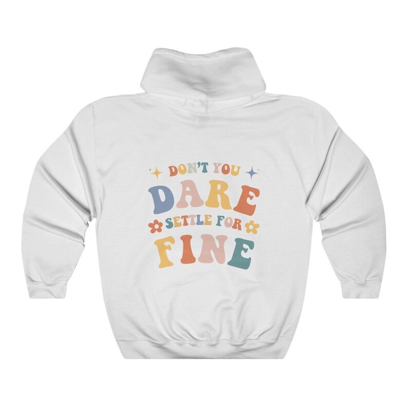 Puede incluir: Sudadera con capucha blanca con el texto "Don't you dare settle for fine" en letras retro de colores.