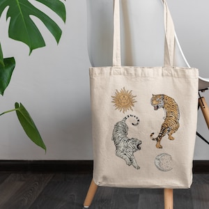 Op de afbeelding: Een beige canvas tote bag met een witte tijger, een oranje tijger, een zon en een maanontwerp.