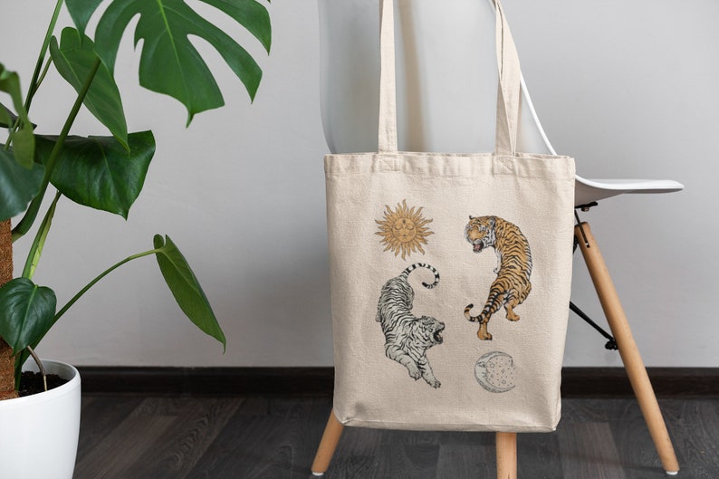Op de afbeelding: Een beige canvas tote bag met een witte tijger, een oranje tijger, een zon en een maanontwerp.