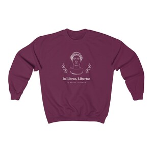 May include: Burgundy sweatshirt with a white graphic of a woman's bust with laurel branches and the text "In Libras, Libertas" and "In books, freedom".