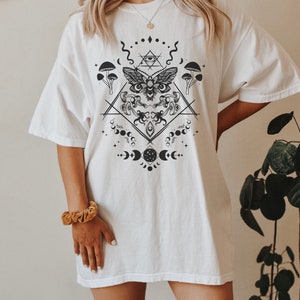 May include: White oversized t-shirt with a black and white graphic print of a moth, mushrooms, moons, and geometric shapes.