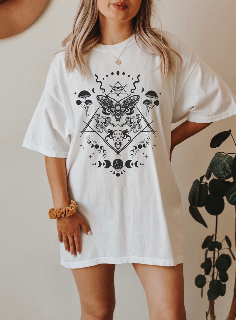 May include: White oversized t-shirt with a black and white graphic print of a moth, mushrooms, moons, and geometric shapes.