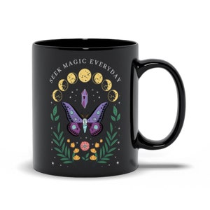 May include: Black ceramic mug with a white design featuring a purple and green moth, a crystal, and a crescent moon phase. The text "Seek Magic Everyday" is written in a circle around the design.
