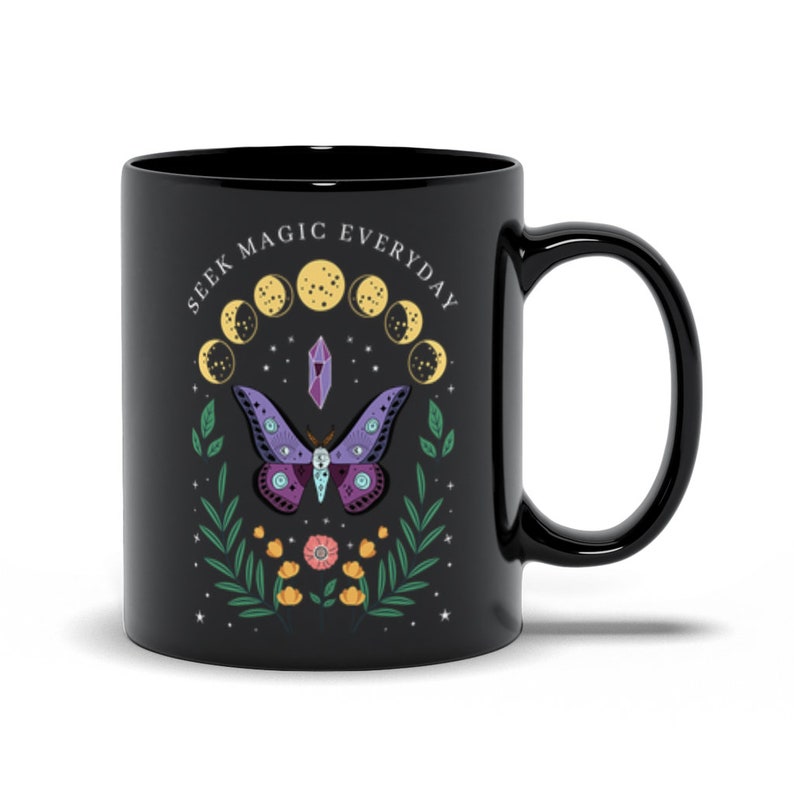 May include: Black ceramic mug with a white design featuring a purple and green moth, a crystal, and a crescent moon phase. The text "Seek Magic Everyday" is written in a circle around the design.