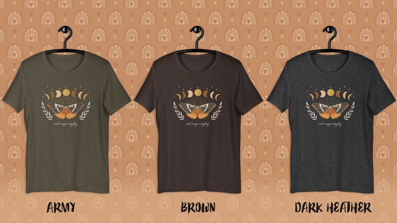 K&ouml;nnte beinhalten: Drei T-Shirts in verschiedenen Farben: Armeegr&uuml;n, Braun und Dunkelgrau meliert. Jedes Shirt zeigt ein Grafikdesign mit einem Schmetterling mit Mondphasen und dem Text "and magic unfolding".