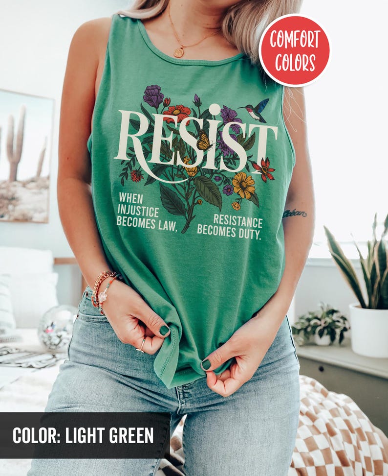 May include: A light green tank top with the word "RESIST" printed in white with a floral design and the text "When injustice becomes law, resistance becomes duty."