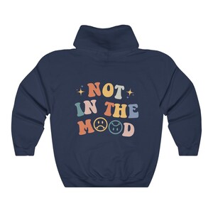 Pu&ograve; includere: Felpa con cappuccio blu navy con il testo "NOT IN THE MOOD" in colori arcobaleno con due emoji di faccina triste.