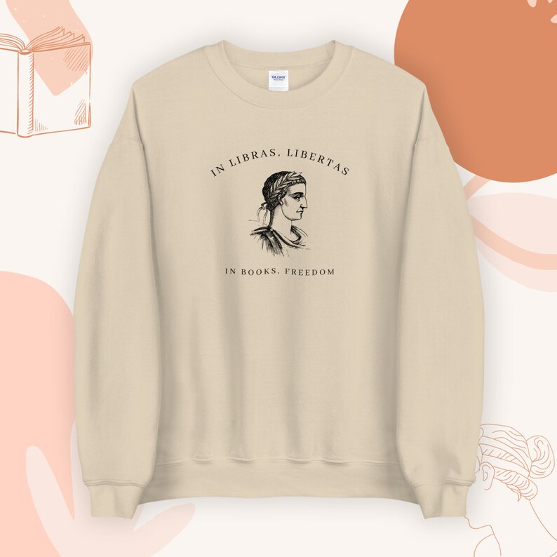 May include: A beige sweatshirt with a black and white illustration of a woman's head and the text "In Libras, Libertas. In Books, Freedom."