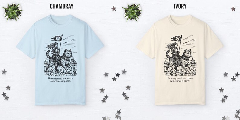 Peut inclure: Deux t-shirts avec un imprim&eacute; graphique d'une femme chevauchant un chat. Le texte sur le t-shirt est "Bravery need not roar - sometimes it purrs." Le t-shirt de gauche est bleu clair et le t-shirt de droite est ivoire.