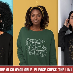 Op de afbeelding: Drie verschillende sweatshirts met verschillende ontwerpen. De eerste sweatshirt is zwart met een gouden maan- en vlinderontwerp. De tweede sweatshirt is groen met een wit paddenstoelontwerp. De derde sweatshirt is zwart met een gouden maan- en paddenstoelontwerp.
