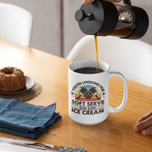 May include: White coffee mug with a retro-style design featuring two pickleball paddles and the text "If you're looking for a soft serve, go get ice cream".