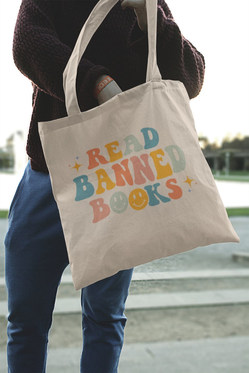 Peut inclure: Un sac fourre-tout beige avec le texte "READ BANNED BOOKS" en couleurs arc-en-ciel avec des smileys.