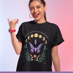 May include: Black t-shirt with a graphic design featuring a purple butterfly, a crystal, and the text "SEEK MAGIC EVERYDAY" in a circle around the design.
