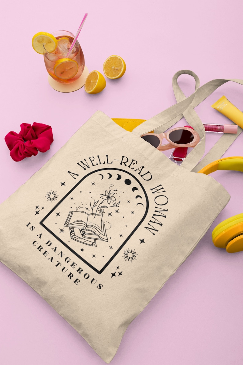 Pode incluir: Bolsa tote bege com texto preto que diz "A well-read woman is a dangerous creature". A bolsa cont&eacute;m &oacute;culos de sol, brilho labial e uma carteira amarela. Uma bebida com rodelas de lim&atilde;o e uma presilha de cabelo vermelha tamb&eacute;m s&atilde;o vis&iacute;veis.