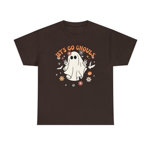 May include: A brown t-shirt with a white ghost graphic and the text "Let's Go Ghouls" in orange and white lettering. The ghost is wearing a flower crown and has peace signs for hands.