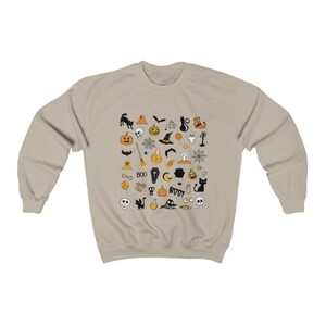 May include: A beige sweatshirt with a Halloween-themed design. The design features a variety of black and orange icons, including pumpkins, bats, ghosts, witches, and skulls.