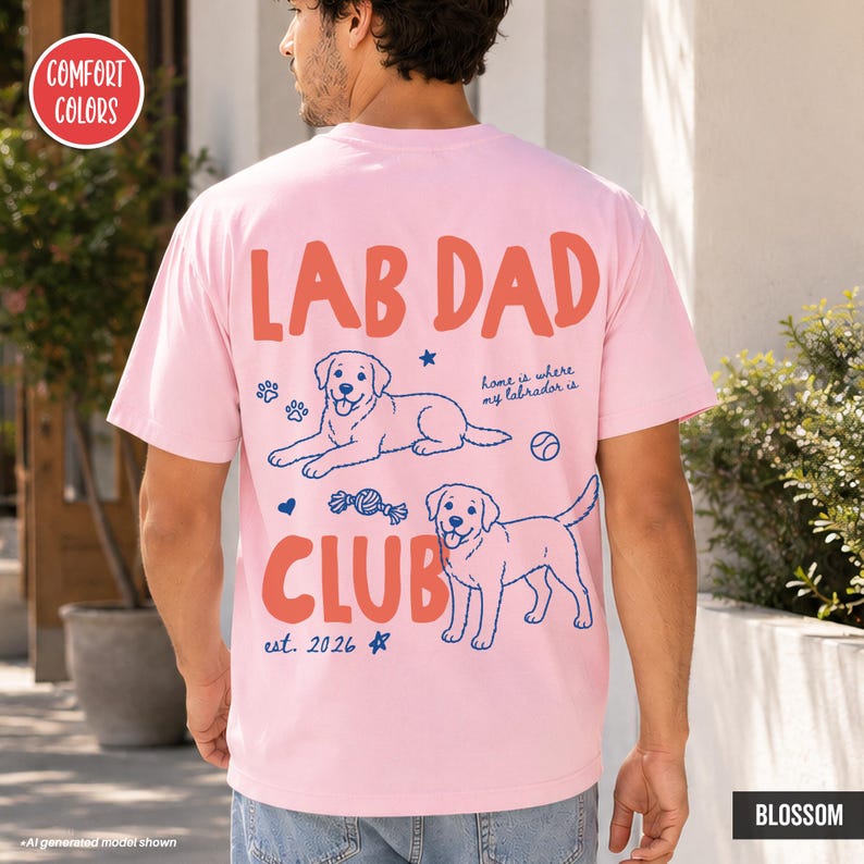 Puede incluir: Una camiseta de manga corta rosa claro con un gr&aacute;fico en la espalda que incluye el texto LAB DAD CLUB, est. 2026, y home is where my labrador is. El dise&ntilde;o muestra dos ilustraciones de Labrador, huellas, una pelota y estrellas.