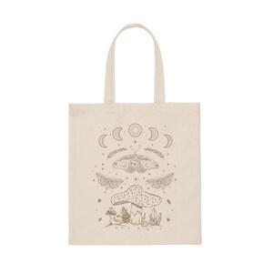 May include: A beige tote bag with a brown design featuring a mushroom, butterflies, and a crescent moon with stars.