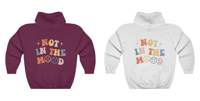 Pu&ograve; includere: Due felpe con cappuccio con il testo "NOT IN THE MOOD" in lettere retr&ograve; colorate e due emoji con facce tristi. Una felpa &egrave; color granata e l'altra &egrave; bianca.