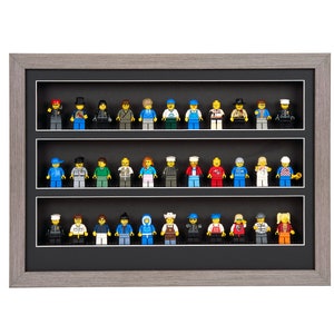 May include: A gray framed display case with three shelves for displaying Lego minifigures. The shelves are black and the minifigures are arranged in rows.