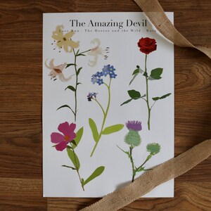 May include: A white poster with the title "The Amazing Devil" and the subtitle "Love Run - The Horror and the Wild Ruin". The poster features illustrations of six different flowers: a red rose, a purple thistle, a pink flower, a blue forget-me-not, and two white lilies.