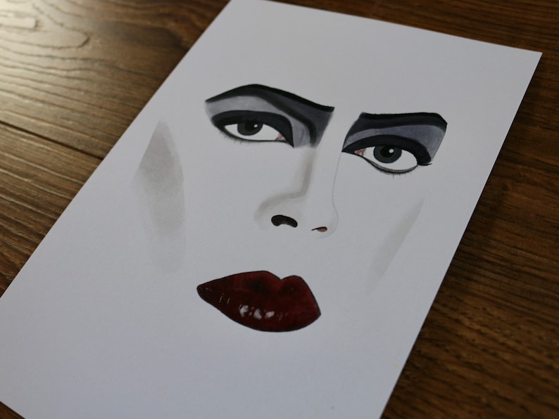 Puede incluir: Un primer plano de una pintura de acuarela de la cara de una persona. La persona tiene sombra de ojos oscura y delineador de ojos oscuro, y sus labios est&aacute;n pintados de un rojo intenso.