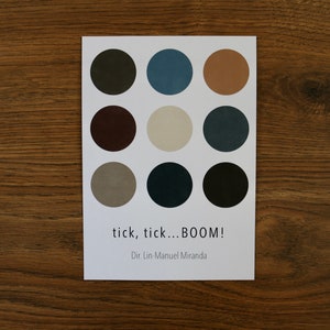 May include: A white card with nine colored circles arranged in three rows. The circles are in shades of brown, gray, and blue. The text "tick, tick...BOOM!" and "Dir. Lin-Manuel Miranda" is printed below the circles.