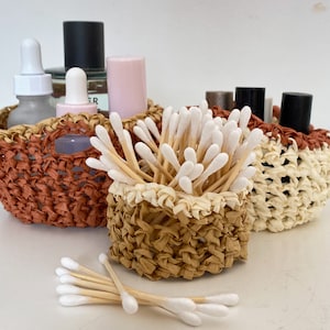 May include: Three woven baskets in brown, beige, and white, filled with cotton swabs and various bottles of toiletries.