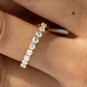 以下が含まれることがあります： 小さな丸い透明なダイヤモンドが並んだ金のバンドリングです。