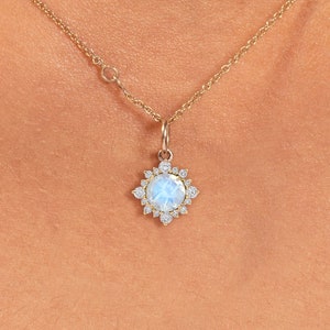 May include: A gold necklace featuring a pendant with a light blue gemstone surrounded by small, clear crystals. The pendant is circular with a starburst design. The necklace is displayed against a white background.