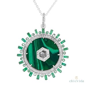 May include: A silver pendant necklace featuring a large, round malachite stone with a central, hexagonal diamond. The pendant is encircled by a ring of small diamonds and emerald-cut emeralds, creating a sunburst design.