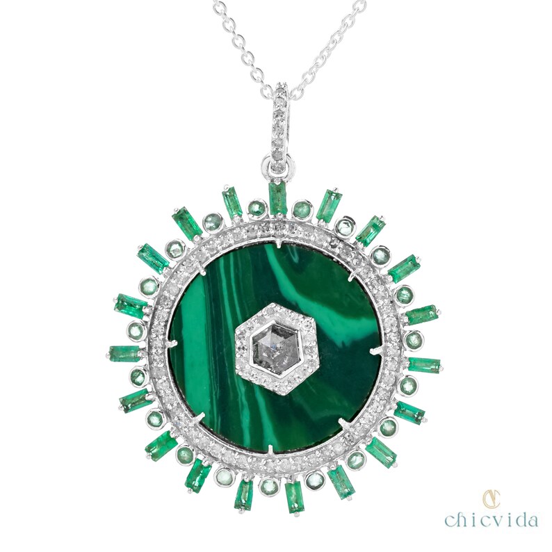 May include: A silver pendant necklace featuring a large, round malachite stone with a central, hexagonal diamond. The pendant is encircled by a ring of small diamonds and emerald-cut emeralds, creating a sunburst design.
