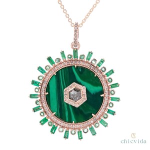 May include: A rose gold pendant necklace featuring a large, round malachite stone with a central hexagonal diamond. The pendant is encircled by a ring of diamonds and emeralds, with emerald accents radiating outwards. The necklace has a delicate chain.