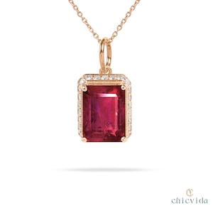 May include: A rose gold pendant necklace featuring a rectangular, deep red gemstone with a halo of small, clear gemstones. The pendant hangs from a delicate chain. The jewelry is set against a white background.