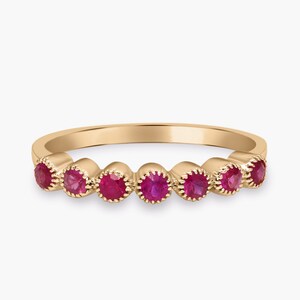 May include: A gold ring with seven vivid red gemstones. Each gemstone is set in a scalloped bezel, giving a delicate appearance. The ring has a smooth, polished band. The gemstones are set in individual, scalloped bezels.