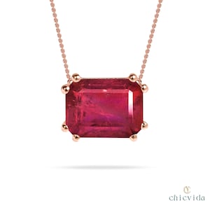 Könnte beinhalten: Halskette aus Roségold mit rechteckigem Rubinanhänger. Der Rubin ist tiefrot, mit kleinen goldenen Akzenten gefasst. Die Kette ist filigran, ebenfalls aus Roségold. Anhänger misst ca. 2 cm x 1,5 cm.