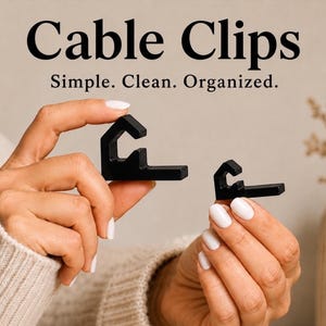 Op de afbeelding: Twee zwarte kabelclips van verschillende groottes, elk met een haakvormige bovenkant en een platte basis. De tekst Cable Clips Simple. Clean. Organized. staat boven de clips. De clips worden vastgehouden om hun vormen te tonen.