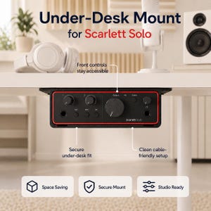 May include: Black under-desk mount for a Scarlett Solo audio interface. The mount has a red trim and includes knobs, inputs, and outputs. Text on the mount reads "Scarlett Solo". The image also shows a white speaker, headphones, and a microphone.