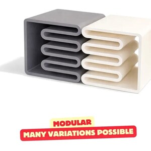 Peut inclure: Deux unités modulaires carrées, une gris foncé et une blanche, chacune présentant une structure interne en forme de U répétée. Sous les unités, une étiquette rectangulaire rouge avec du texte jaune indique : MODULAR MANY VARIATIONS POSSIBLE.