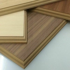 May include: Close-up of several wooden frames in varying shades of brown and tan. The frames have a decorative edge and are arranged at different angles, showcasing the wood grain and texture. The background is white.